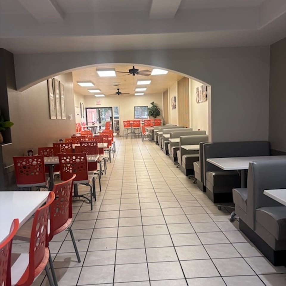 Bright casual restaurant dining room with red chairs, gray booths, tiled floors, ceiling fans, and tables extending toward the entrance.